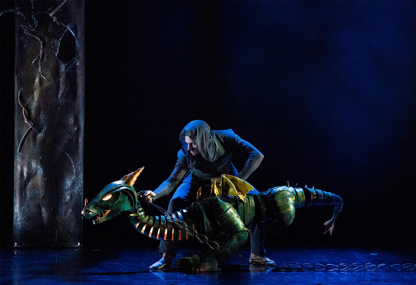 A dancer holding a dragon puppet on stage.