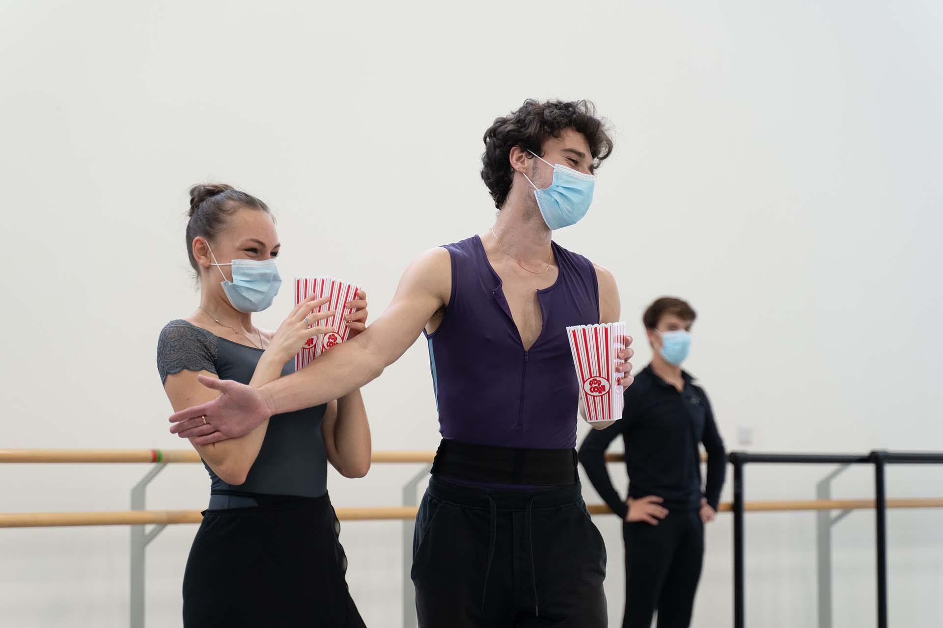 One dancer holds another back while they both hold popcorn