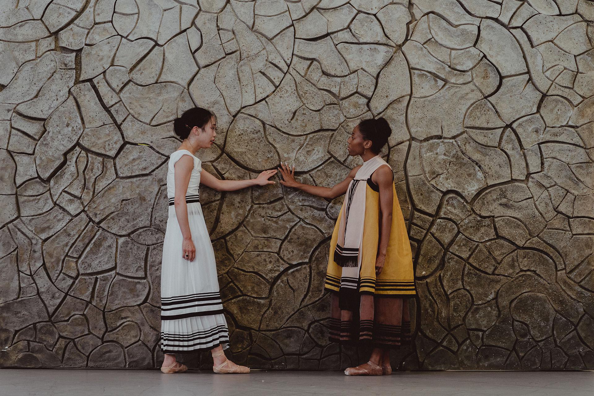 Two dancers hold their hands against a dry cracked wall