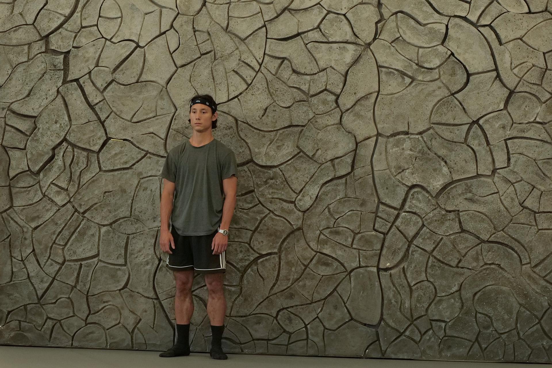 Dancer stands in front of a dry, cracked wall