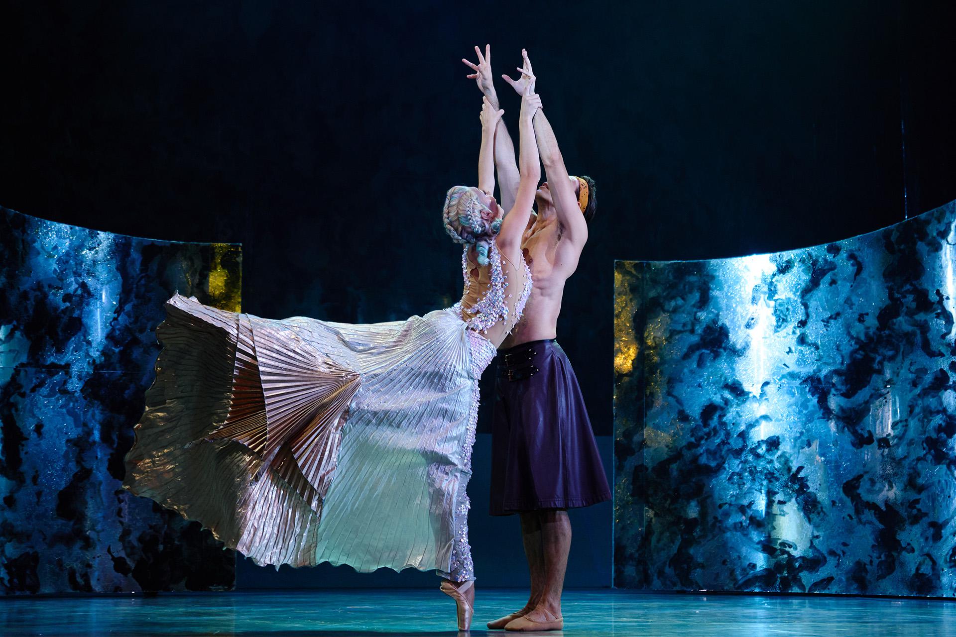 Man reaching up while a female mermaid with tail flowing behind her holds his wrists
