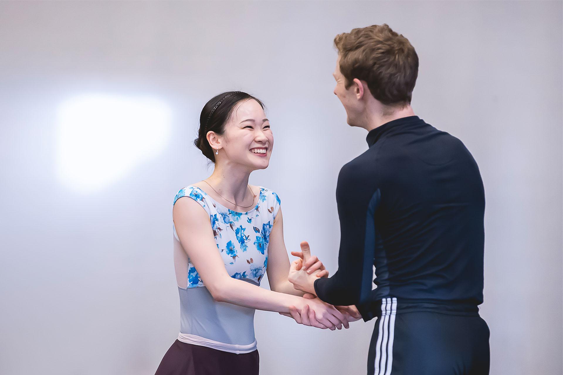 Dancers in rehearsals smiling as they hold hands facing one another.