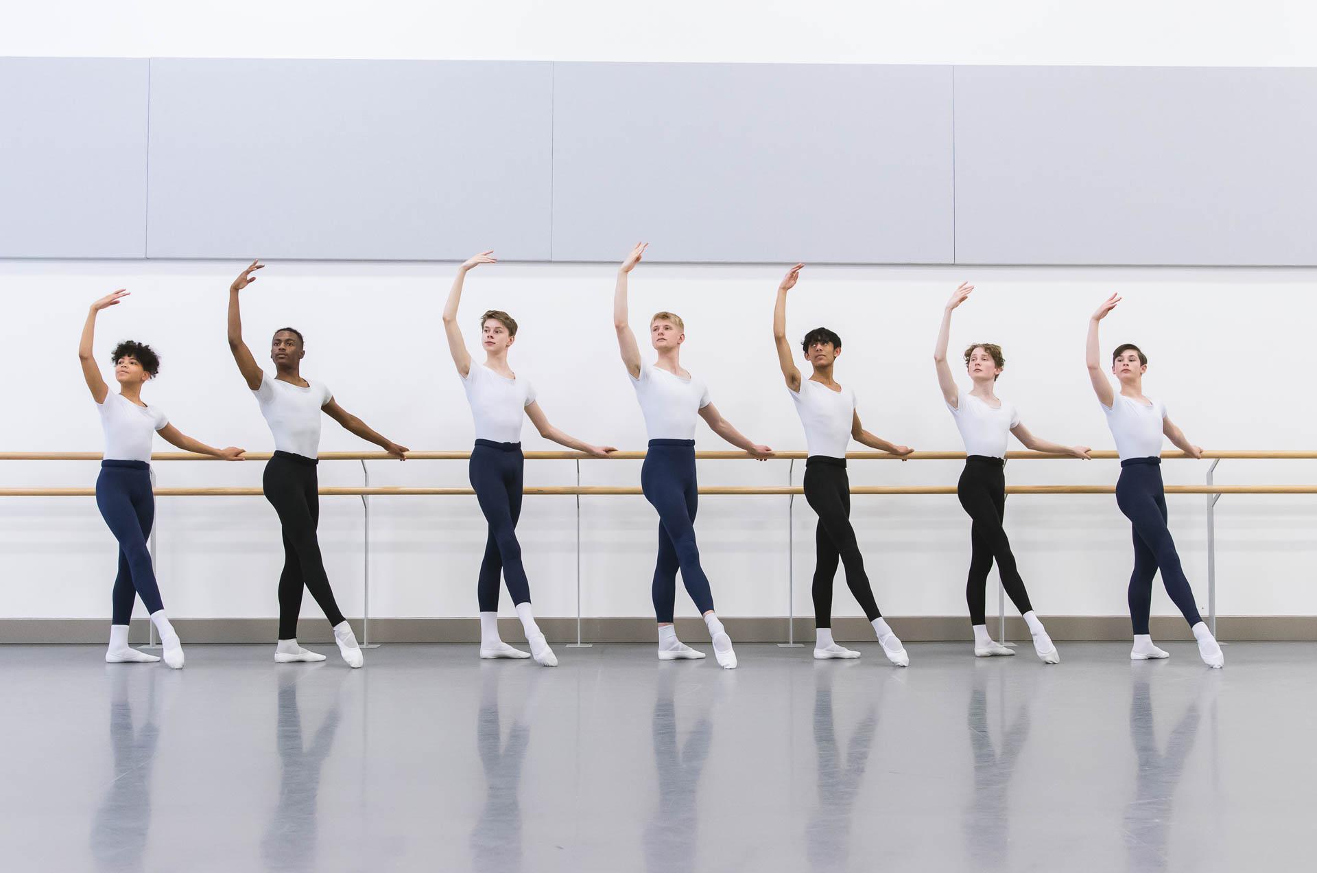 Seven male dancers stood at the bar with one arm raised