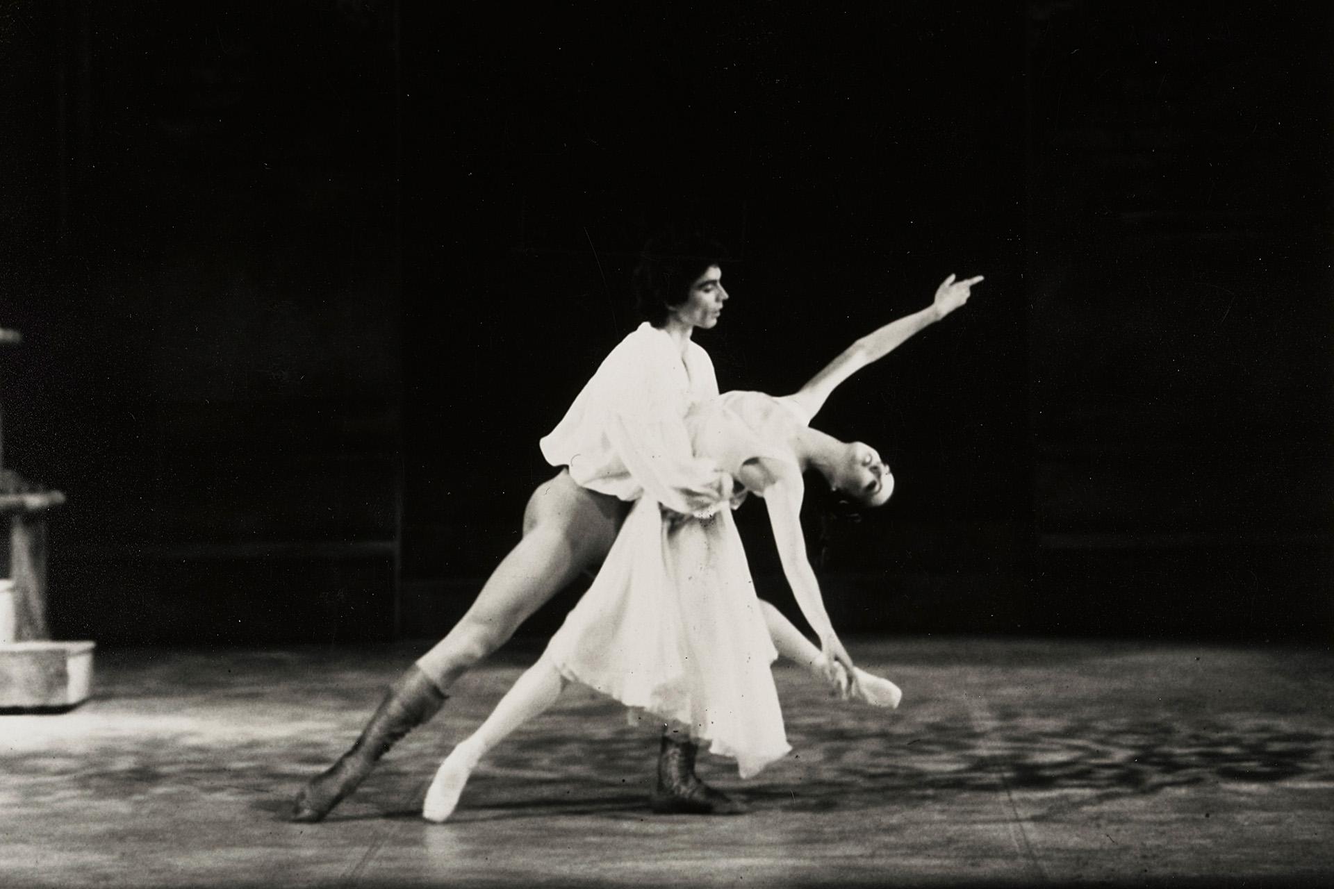 Two dancers in a classical pose. The female dancer stretches out her arms and leans back in a classical pose whilst the male dancer holds her waist