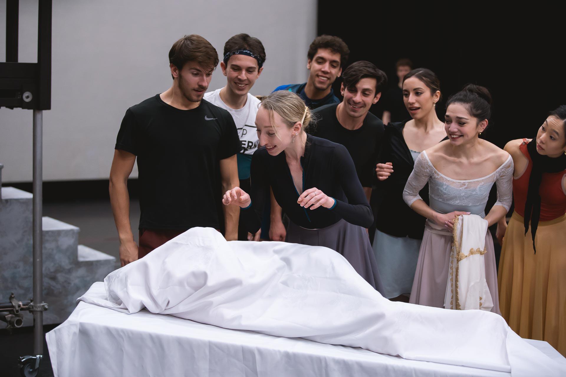A group of dancers stood over a bed