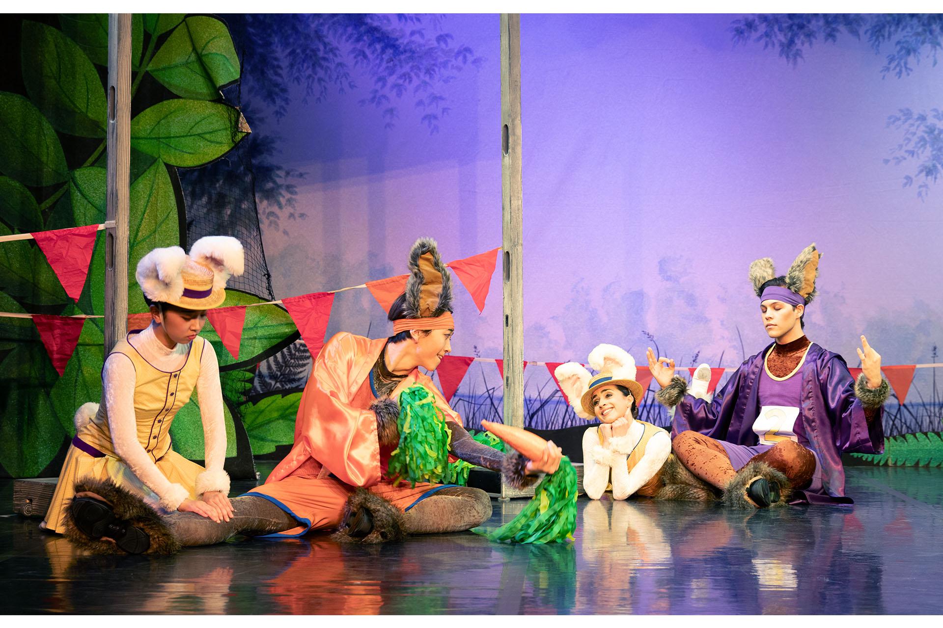 Dancers dressed as bunnies. One dancer checking another dancers leg, middle dancer holding two carrot stick pom poms, another dancer gazing in adoration and the last dancer meditating