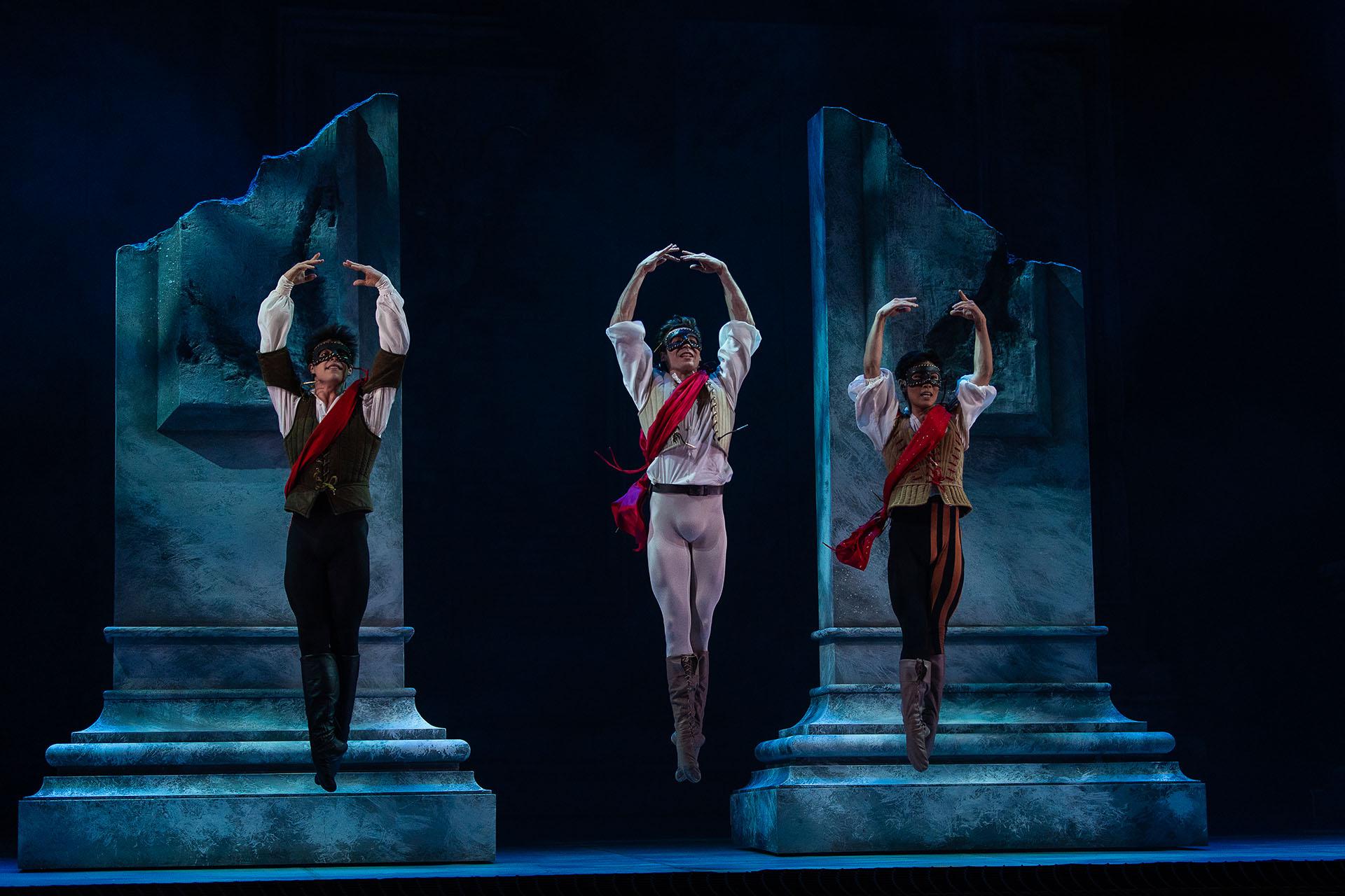 Three men wearing black masks and red sashes jump straight up, their feet together, and their hands above their heads
