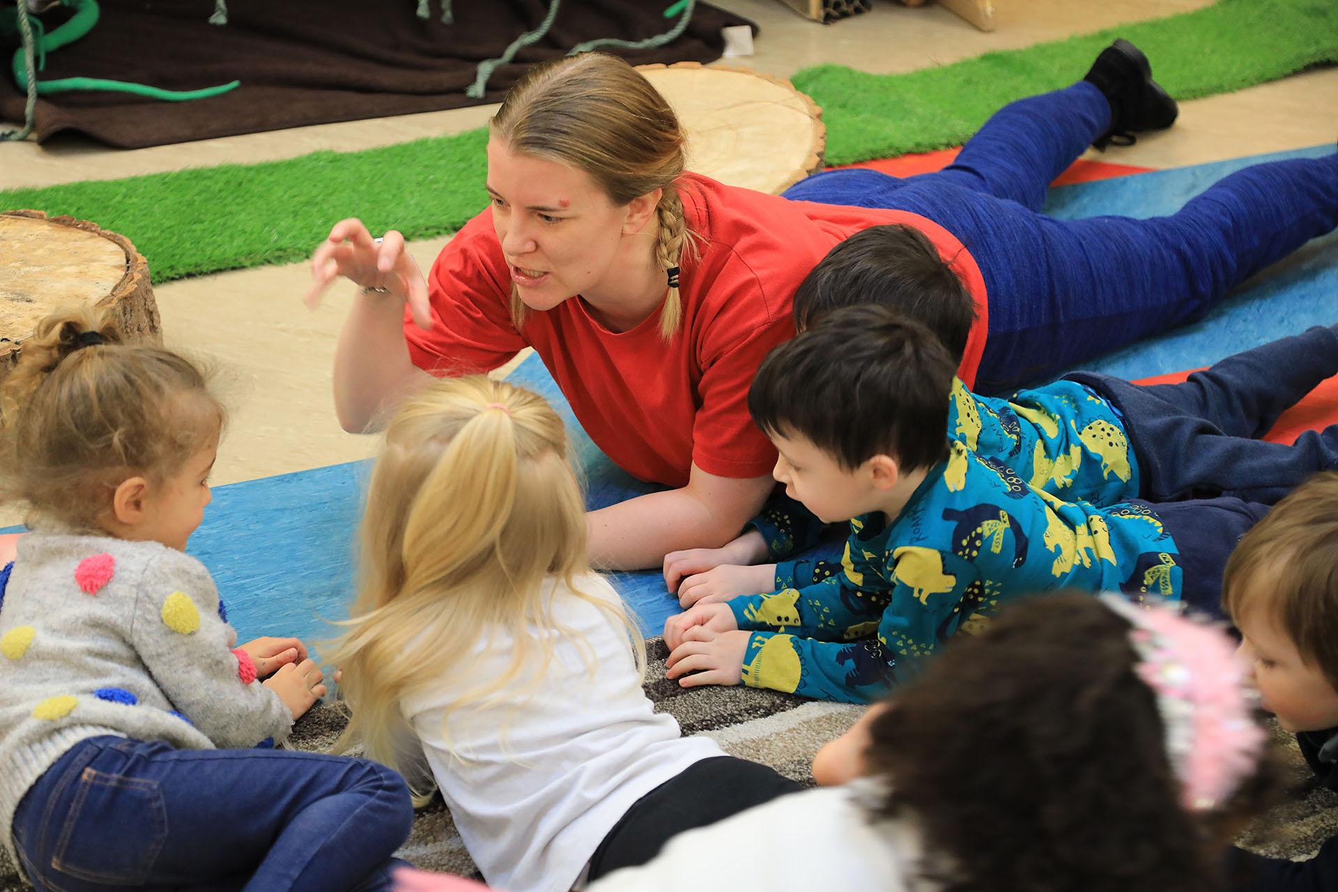 A group of children lay on their bellies facing each other and making claws with their hands