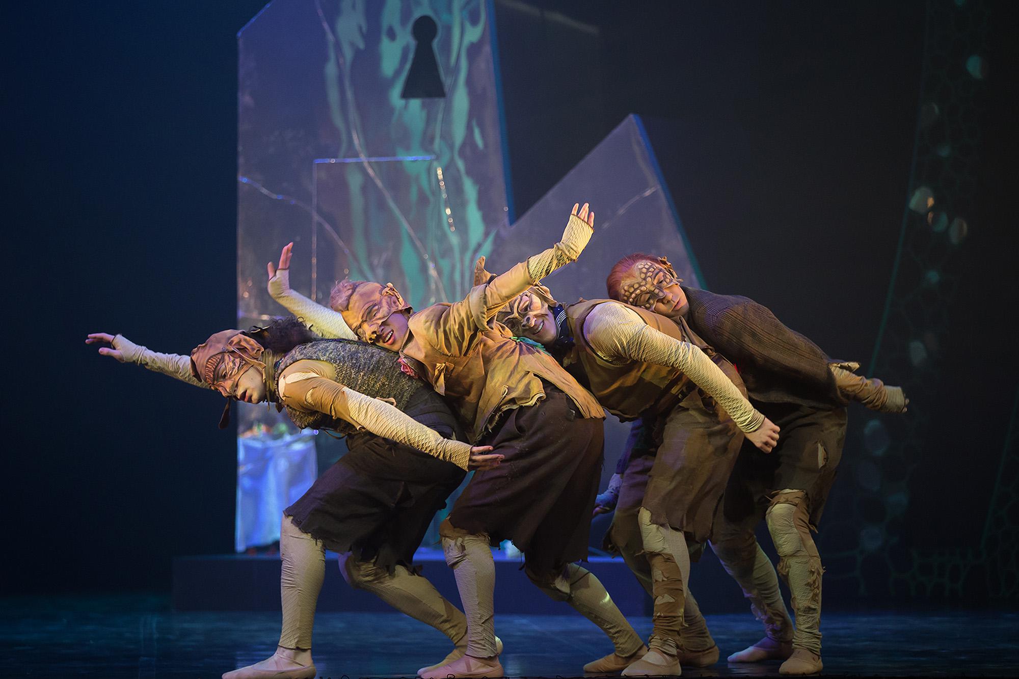 Four dancers dressed as goblins on stage all leant on each other striding across the stage.