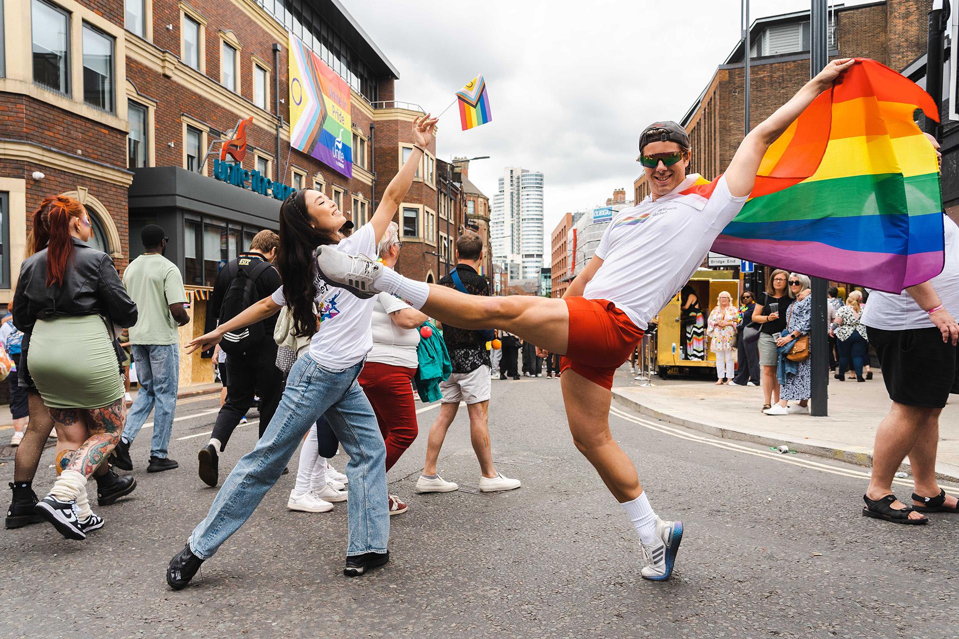 Northern Ballet dancers at Pride 2024, waving the Pride flag,  and in traditional ballet poses
