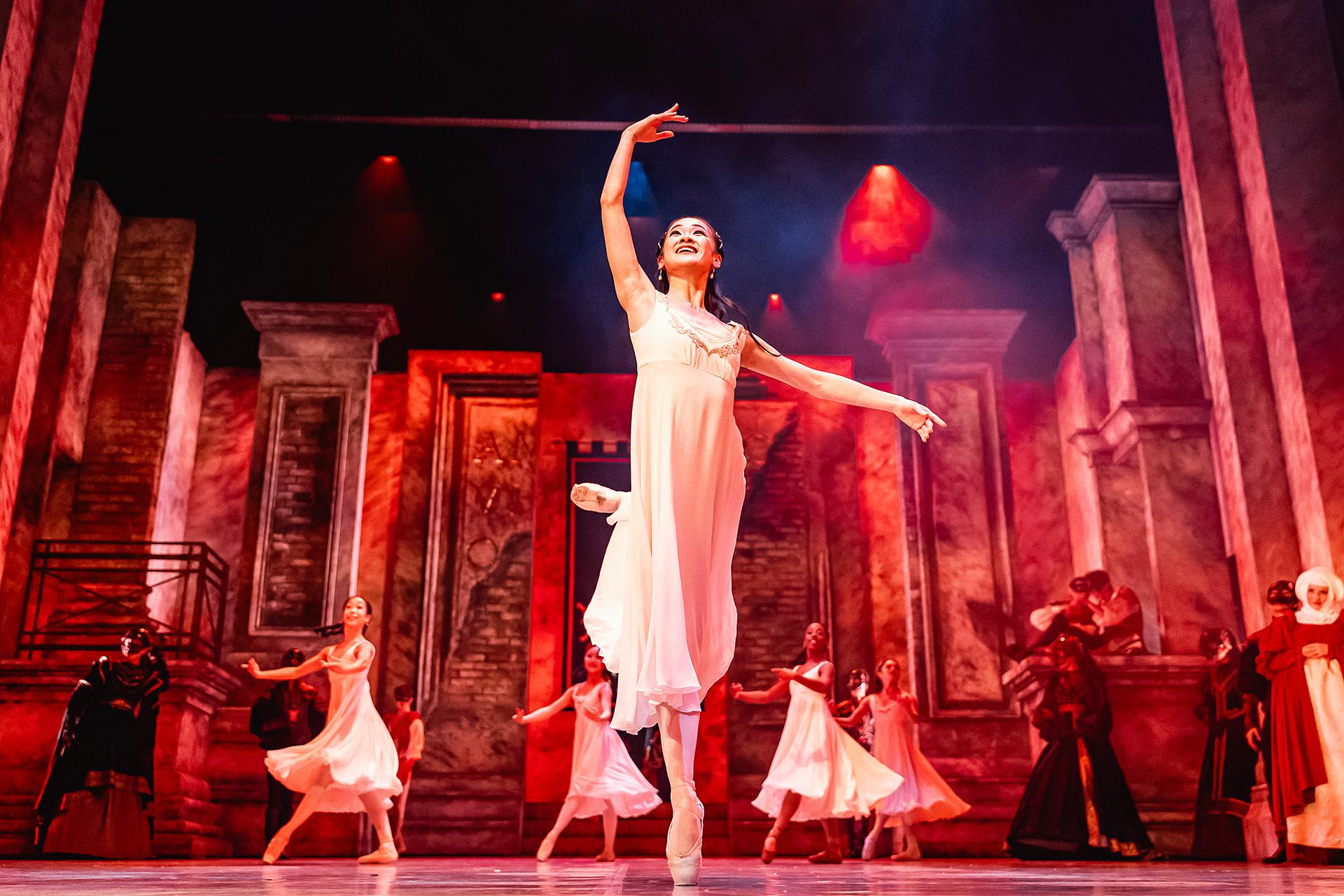 Juliet dressed in a white shift ands en pointe against a dramatically lit set