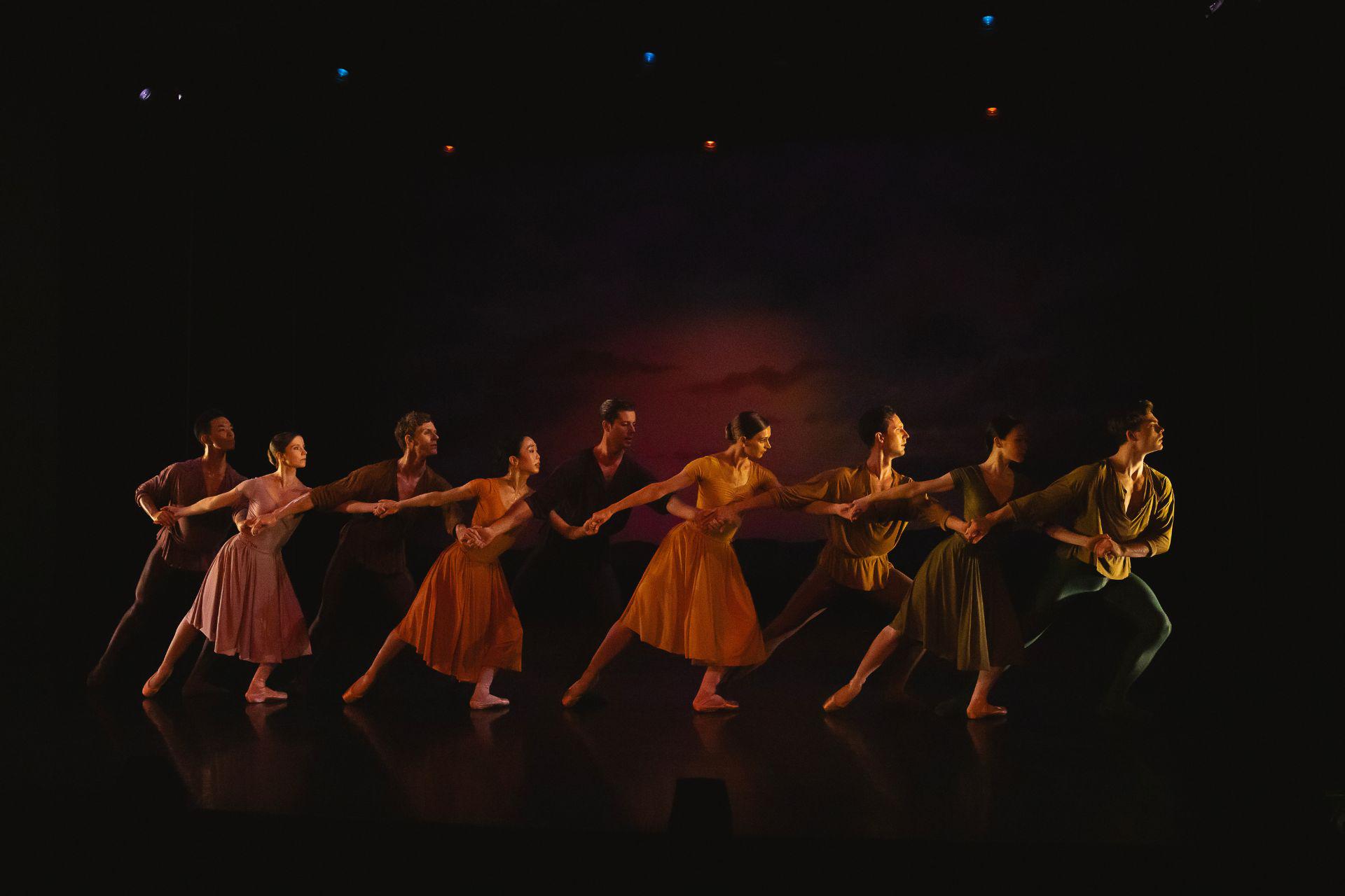 Northern Ballet dancers stand in a line across the stage, holding hands and interlocking arms