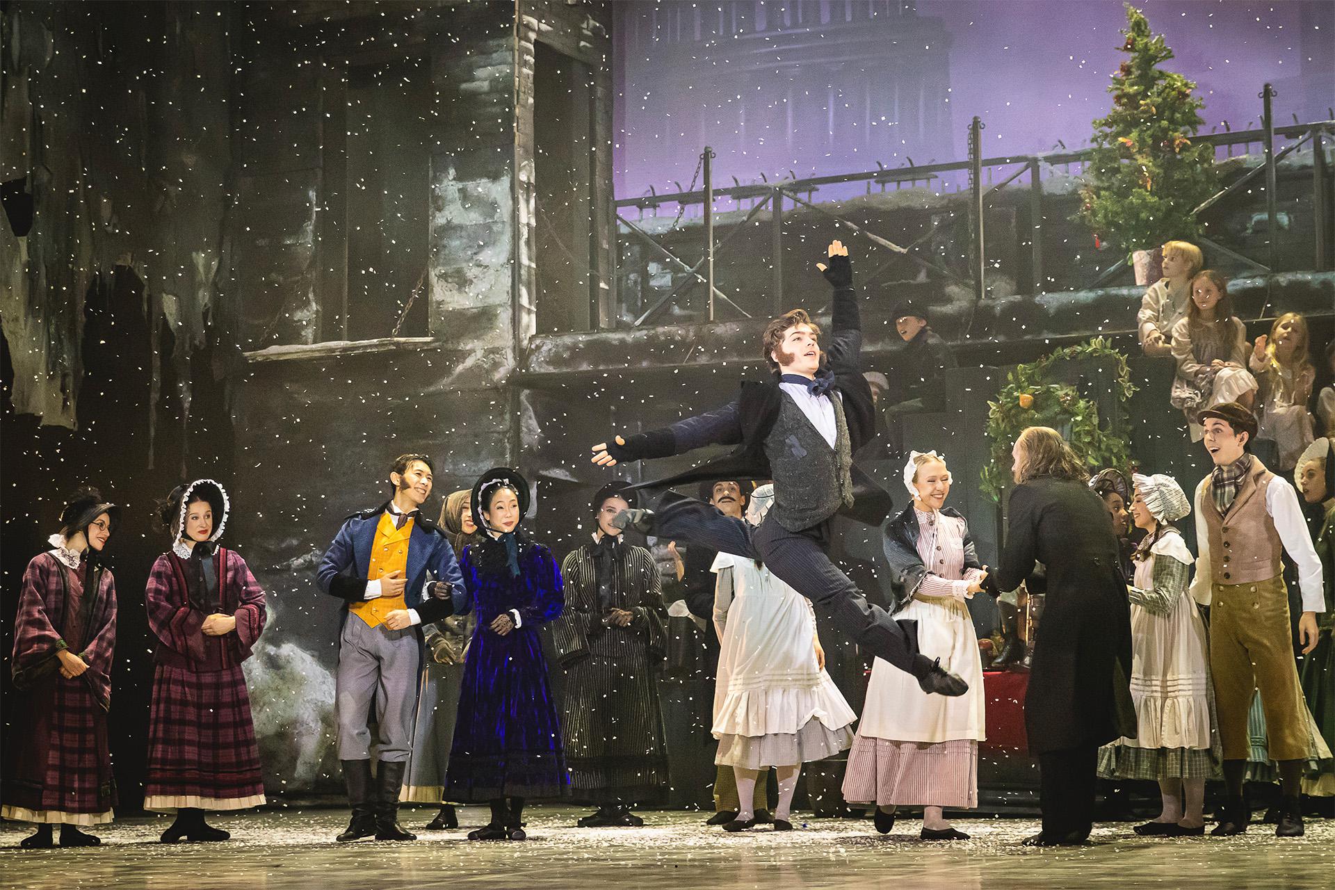 Bob Cratchit leaps into the air as snow falls and townspeople watch on in delight