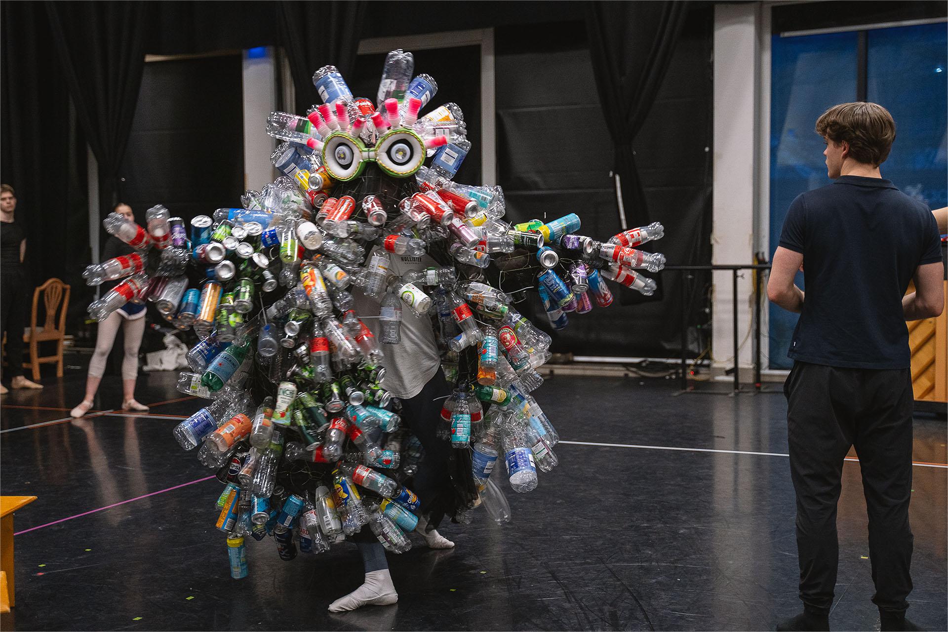 Rehearsing in the trash monster costume, covered in discarded bottles and cans