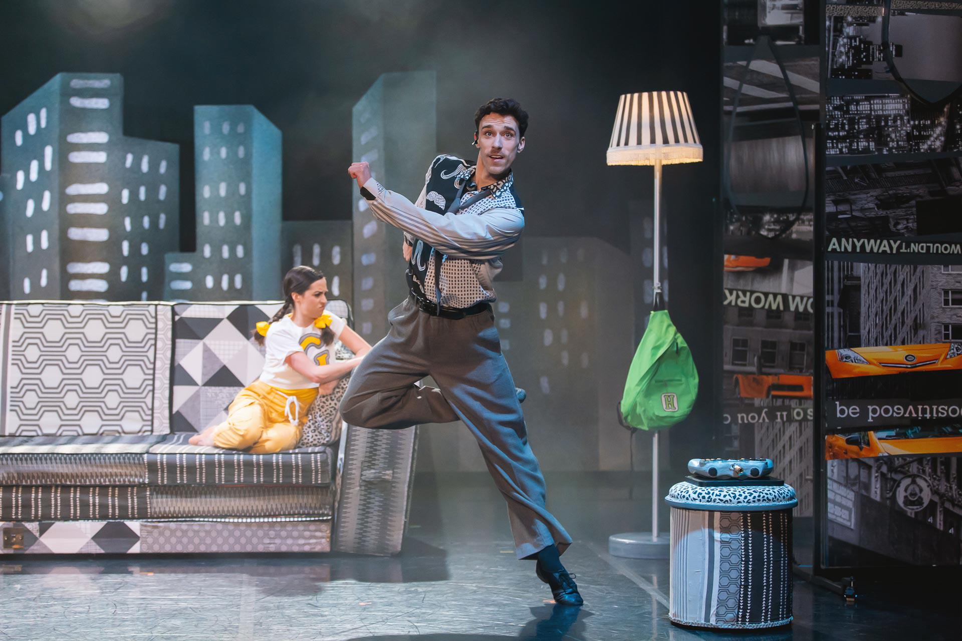 A dancer on stage dressed in grey stood on one leg