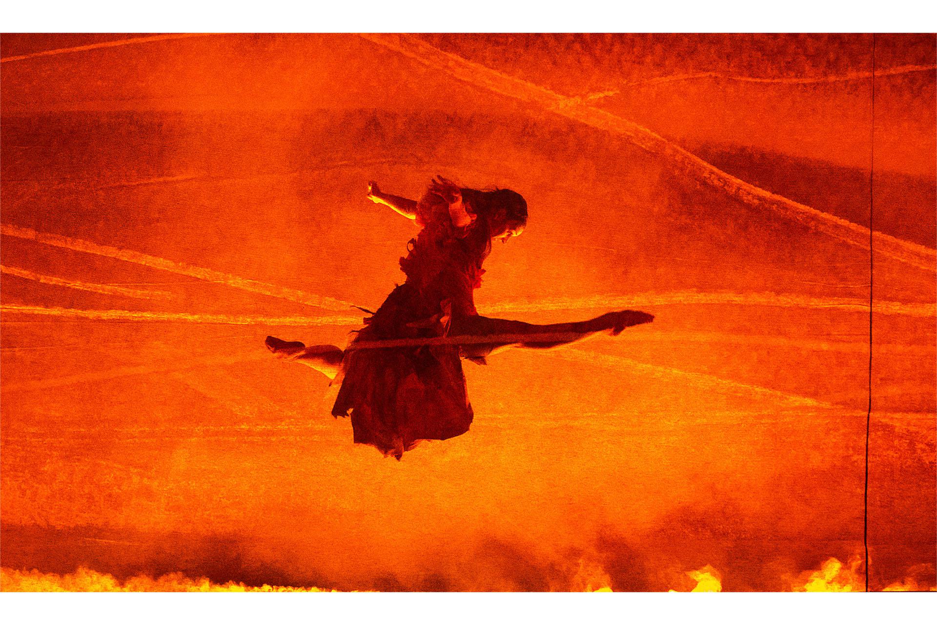 Lit by the orange hue of flames, a dancer performs a great leap