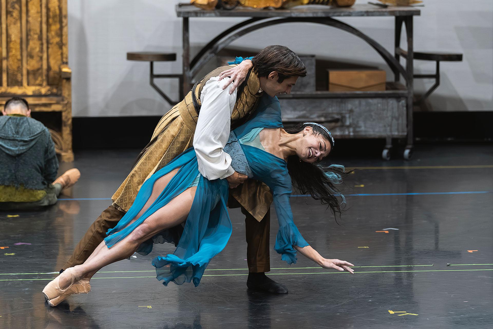 A woman in blue holds her body straight while a man holds her by the waist just above the floor