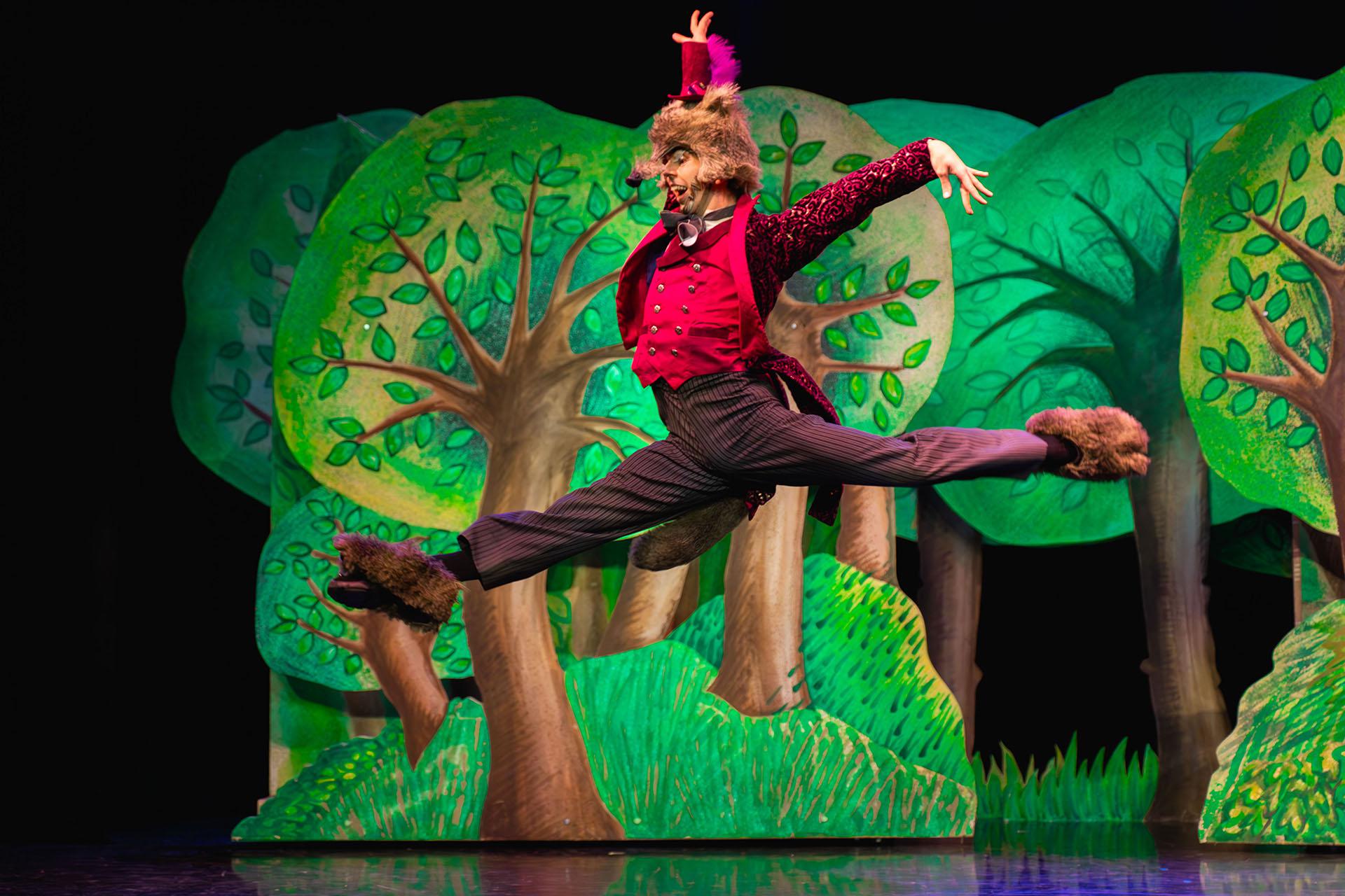 The wolf, dressed in his red waistcoat, velvet jack and high trousers leaps high in a grand jete