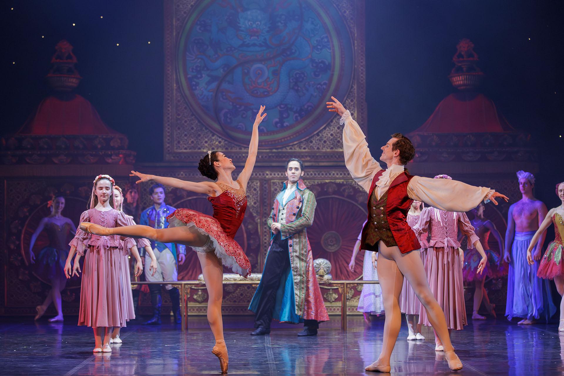 The Sugar Plum Fairy and Cavalier, dressed in deep reds, dance with each other looking at one another