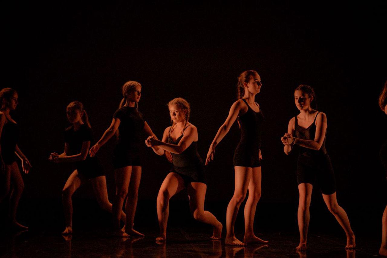 Dancers stood in a line, alternating between hands outstretched facing forward and stood sideways