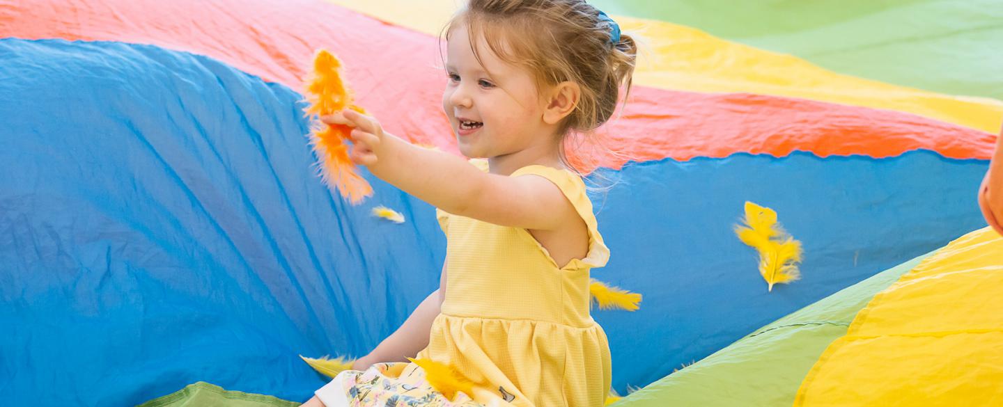 Little girl in a rainbow parachute playing with a feather