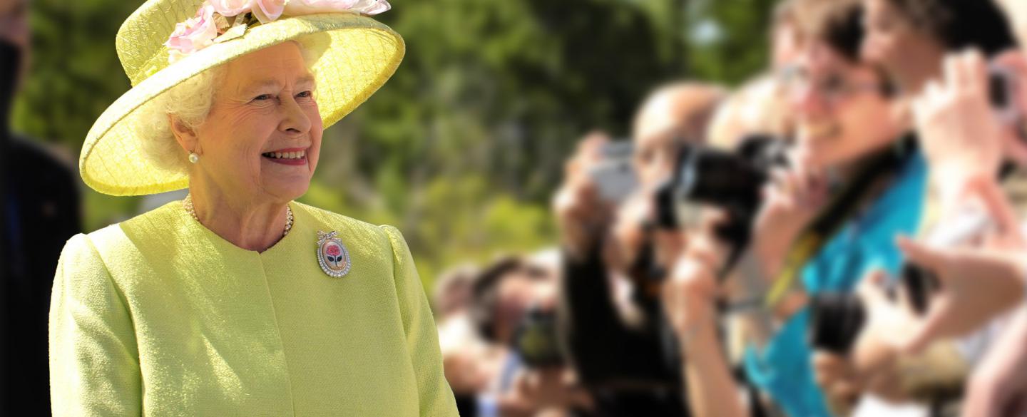 Queen Elizabeth II in a yellow/green outfit standing in front of photographers