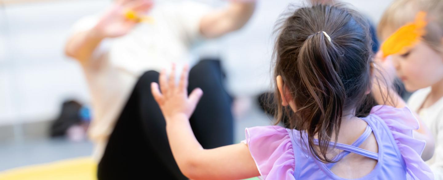 A little girl in a purple leotard reaching to her dance teacher in class