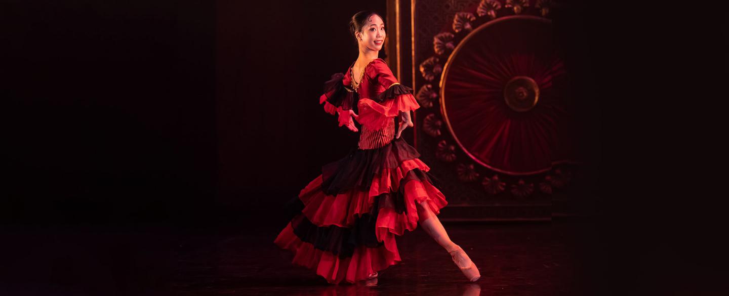 Woman with dark hair tied up dancing in a flowing black and red dress