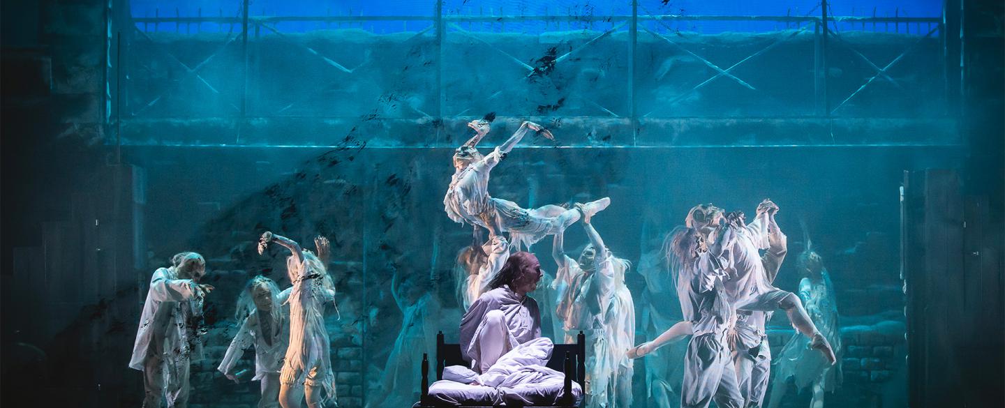 Scrooges sits up in his bed as wraiths dance behind him