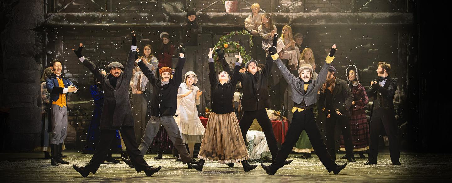 Townspeople dance with their arms in the air and on their heels as snow falls.