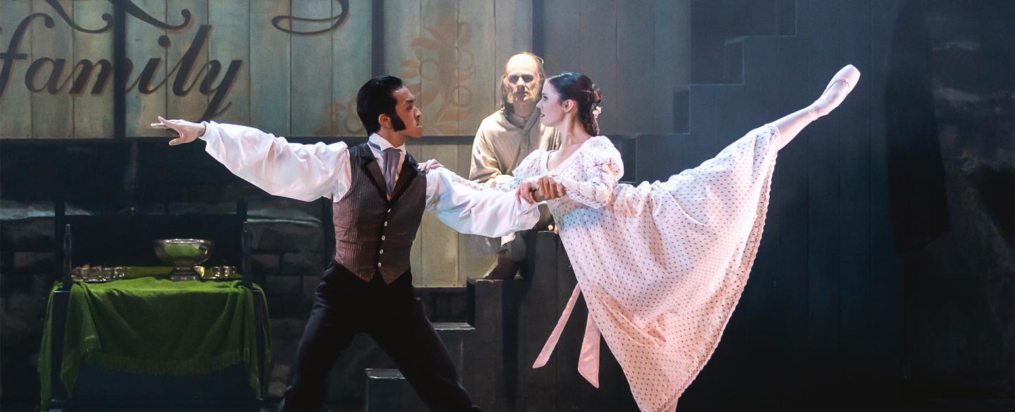 Two dancers on stage, one with arms outstretched and the other stood on pointe with one leg raised