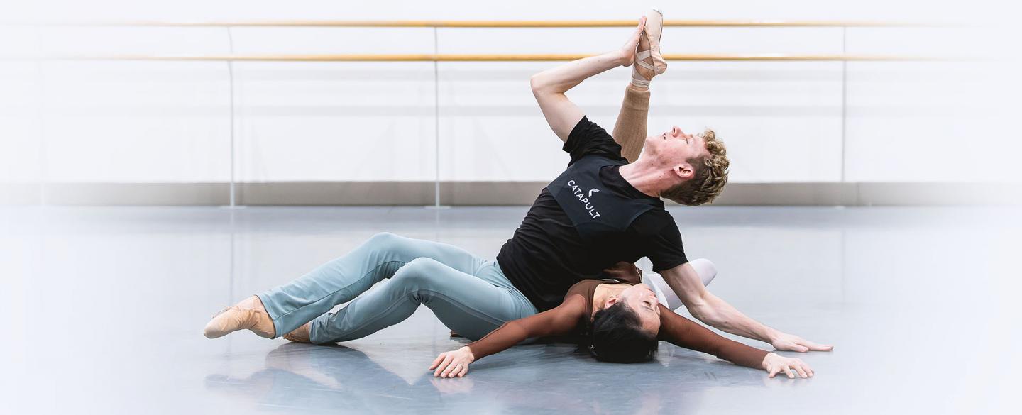 On the studio floor a female dancer lies back, a male dancer leans against her torso