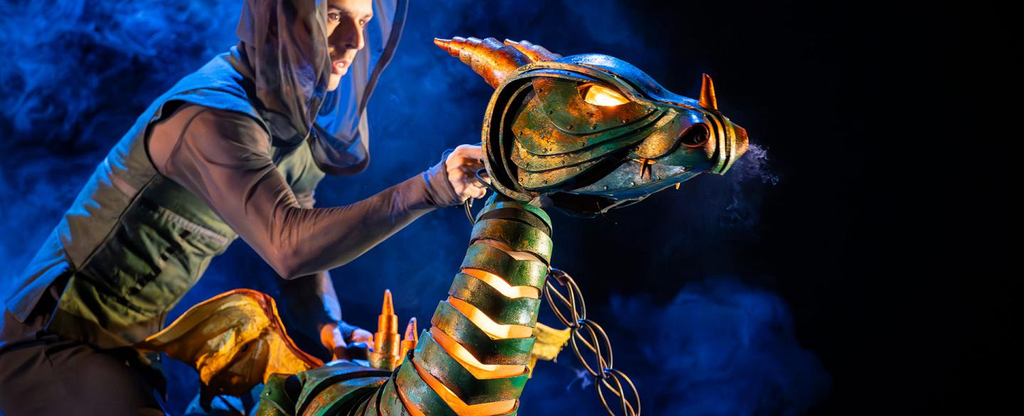 A young dragon, his eyes glowing and light visible through his scales; chained tied to his neck and a puppeteer posing him dramatically.