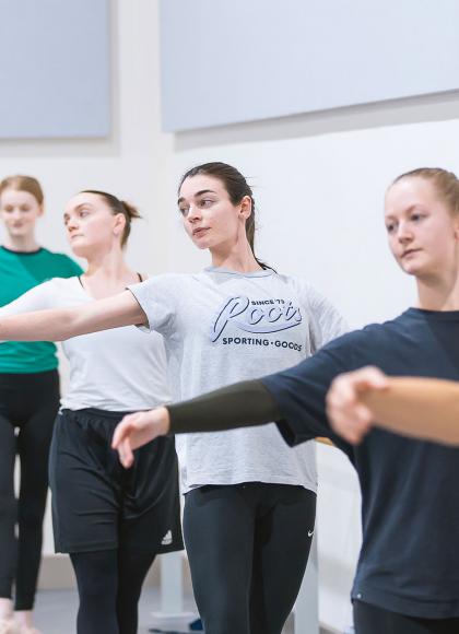 Student dancers at the barre, holding on with one hand, their other arm outstretched