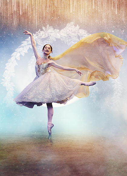 Against a blue and golden fantasy background, a woman stands on one pointed foot, one hand in the air, her other leg balanced elegantly behind her as her dress flows behind her