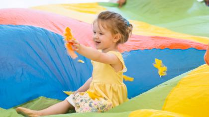 Little girl in a rainbow parachute playing with a feather