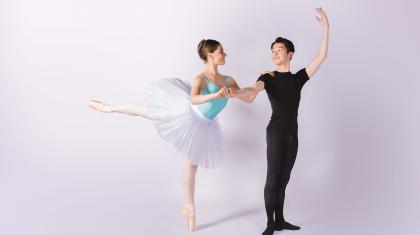 A female student in a white tutu stood on pointe holding the arm of a male student dressed in black