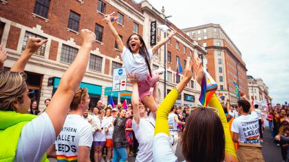 Laughing woman with long dark hair lifted by overhead with her arms raised in celebration