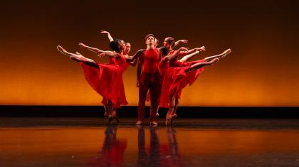 A male dancer stood in the middle of group of dancers in warm red and orange tones