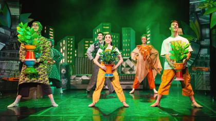 Dancers stood in a row holding potted plants in a soft green light