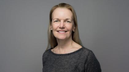 A headshot of a white women with blonde hair wearing a black top smiling to camera against a grey background.