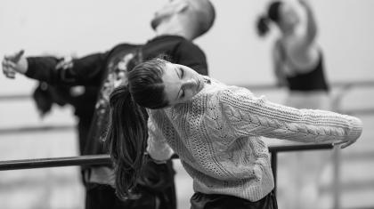 Monochrome image of students practicing at the barre, leaning back and holding their pose
