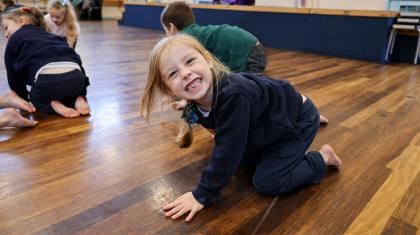 Young student in school hall giving a toothy smile directly at the camera as they stomp on the floor
